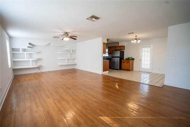 unfurnished living room with built in features, a textured ceiling, ceiling fan with notable chandelier, and light hardwood / wood-style flooring