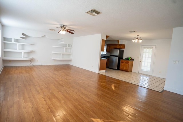 unfurnished living room featuring ceiling fan with notable chandelier, light wood-type flooring, and a textured ceiling