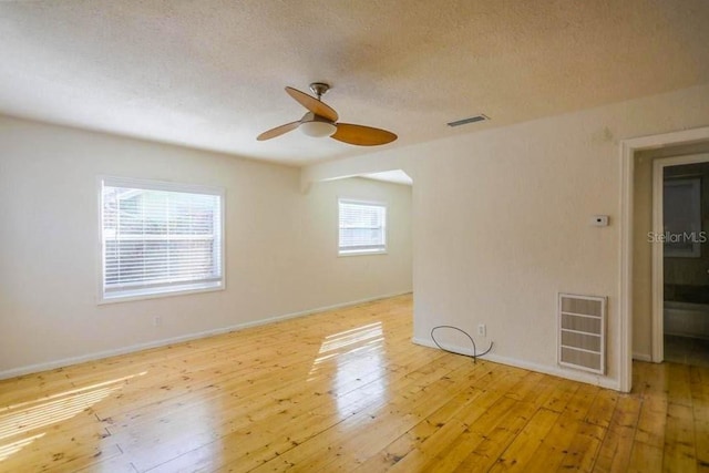 spare room with ceiling fan, light hardwood / wood-style floors, a textured ceiling, and a wealth of natural light