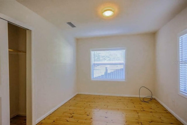 unfurnished bedroom featuring a closet, light hardwood / wood-style floors, and multiple windows