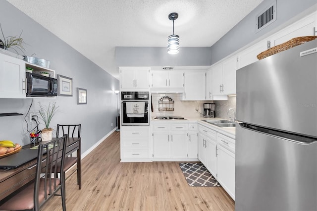 kitchen with backsplash, black appliances, white cabinets, light wood-type flooring, and decorative light fixtures