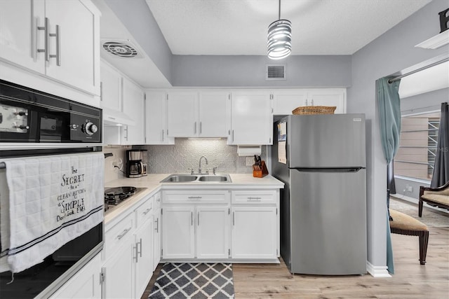 kitchen with light wood-type flooring, stainless steel appliances, sink, white cabinetry, and hanging light fixtures