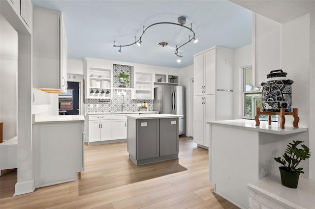 kitchen featuring stainless steel fridge, white cabinetry, a kitchen island, light hardwood / wood-style floors, and decorative backsplash