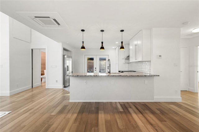 kitchen with sink, kitchen peninsula, white cabinetry, light stone counters, and stainless steel fridge with ice dispenser