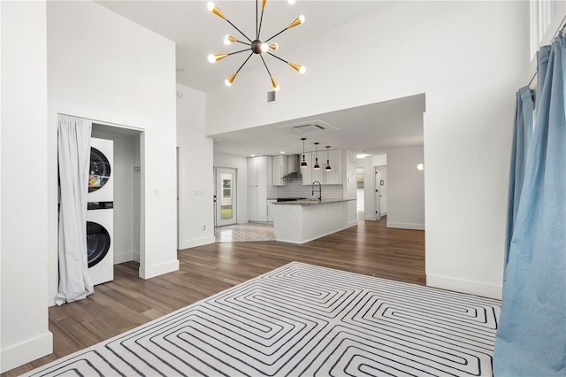 living room featuring dark wood-type flooring, a high ceiling, an inviting chandelier, sink, and stacked washer / drying machine