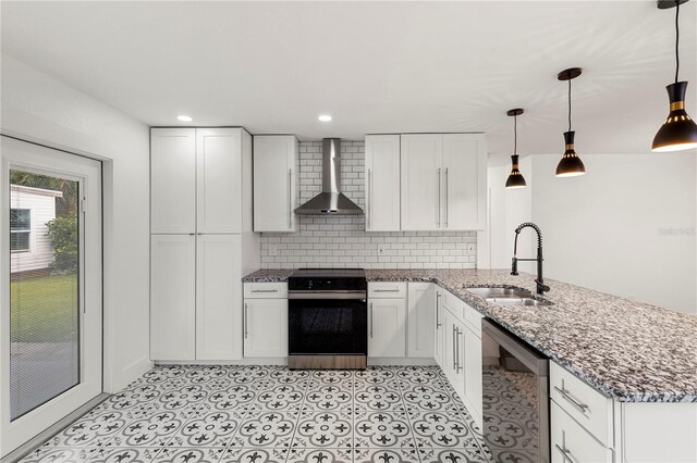 kitchen featuring pendant lighting, white cabinets, wall chimney range hood, sink, and stainless steel appliances