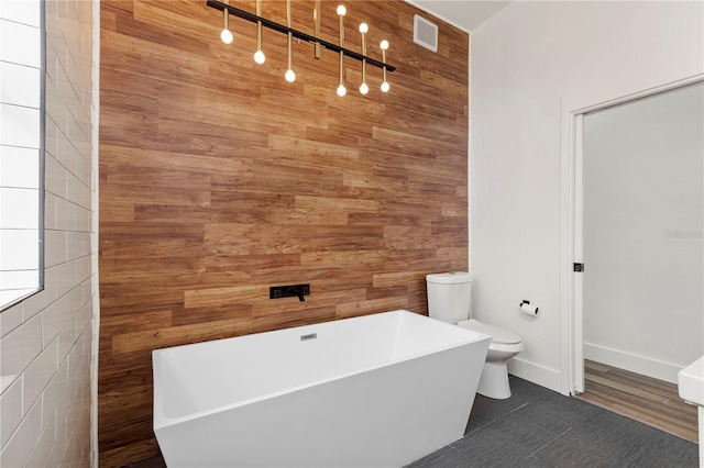 bathroom featuring tile patterned flooring, toilet, a bathtub, and wood walls