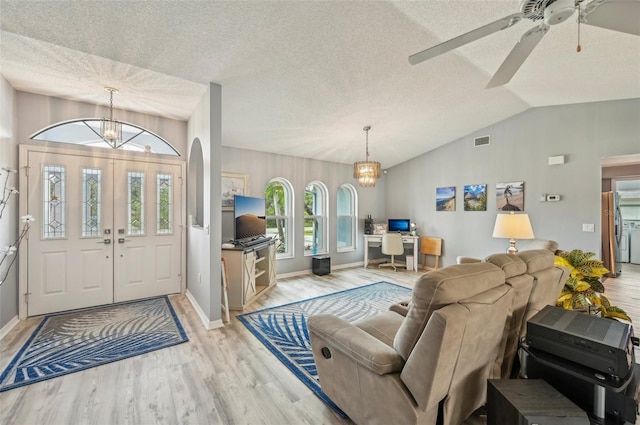 foyer featuring lofted ceiling, ceiling fan with notable chandelier, light hardwood / wood-style floors, and a textured ceiling