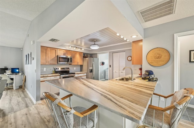 kitchen with sink, light hardwood / wood-style flooring, stainless steel appliances, and kitchen peninsula