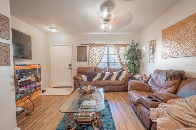 living room featuring ceiling fan, a fireplace, a textured ceiling, and light wood-type flooring