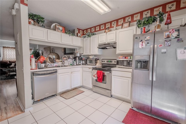 kitchen featuring appliances with stainless steel finishes, a textured ceiling, sink, light tile patterned floors, and white cabinetry