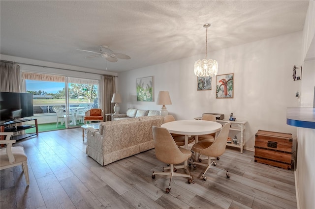 living room with ceiling fan with notable chandelier, light hardwood / wood-style floors, and a textured ceiling