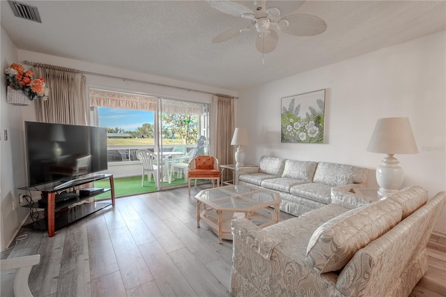 living room with ceiling fan, a textured ceiling, and light hardwood / wood-style flooring