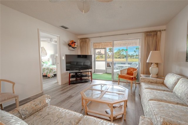 living room featuring a textured ceiling, light wood-type flooring, and ceiling fan