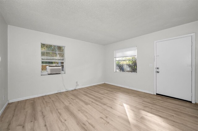 empty room featuring light hardwood / wood-style flooring, cooling unit, and a textured ceiling