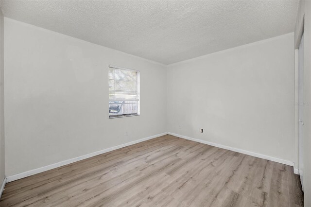 empty room with a textured ceiling, light wood-type flooring, and baseboards