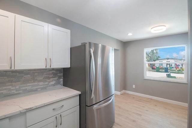 kitchen featuring light hardwood / wood-style flooring, stainless steel refrigerator, light stone counters, tasteful backsplash, and white cabinets