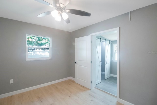 unfurnished room with ceiling fan, a barn door, light hardwood / wood-style floors, and a wealth of natural light