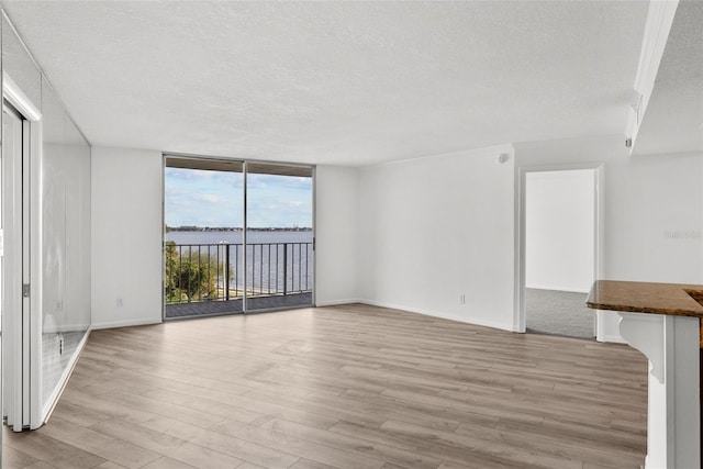 unfurnished living room with a textured ceiling, light wood-type flooring, a water view, and expansive windows