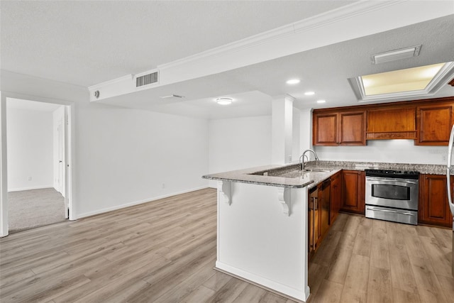 kitchen with a kitchen bar, kitchen peninsula, stainless steel range, sink, and light hardwood / wood-style floors