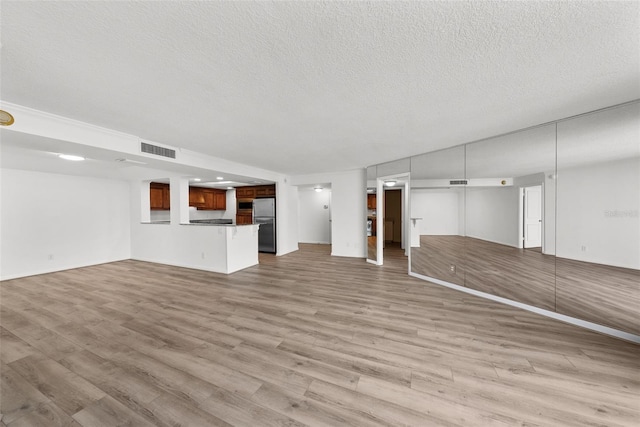 unfurnished living room featuring a textured ceiling and light hardwood / wood-style flooring