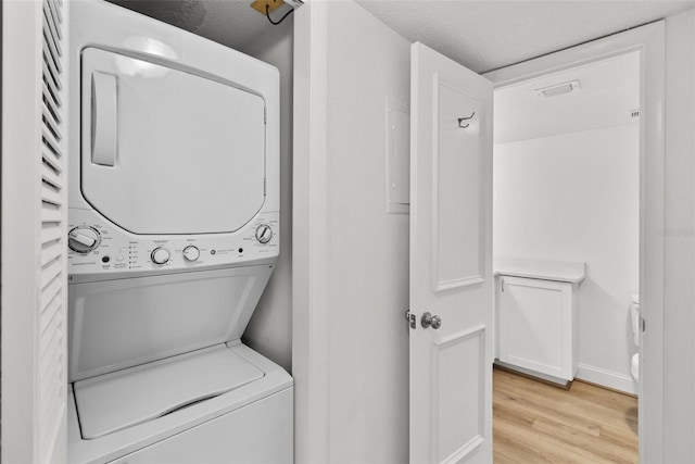 washroom with light hardwood / wood-style flooring, stacked washing maching and dryer, and a textured ceiling