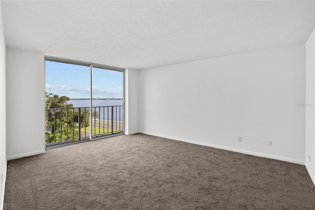 empty room with a water view, dark carpet, a textured ceiling, and a wall of windows