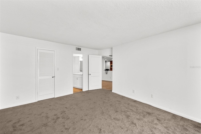 unfurnished bedroom featuring carpet flooring, a textured ceiling, ensuite bath, and a closet