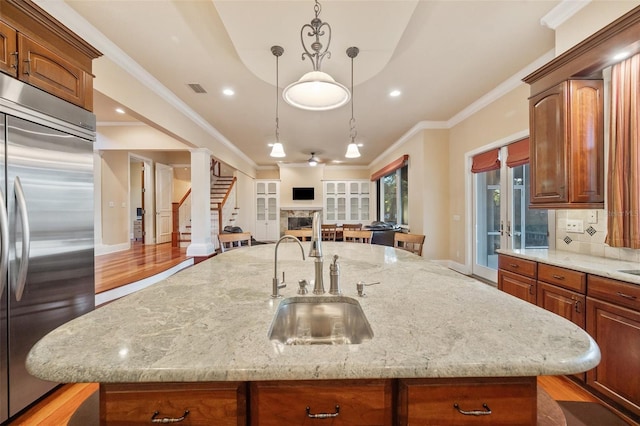 kitchen featuring stainless steel built in refrigerator, sink, pendant lighting, a center island with sink, and light hardwood / wood-style floors