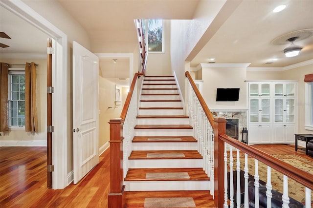 staircase with hardwood / wood-style floors, crown molding, and a fireplace