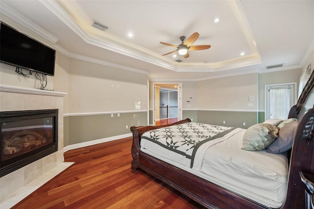 bedroom with ceiling fan, a raised ceiling, hardwood / wood-style floors, a fireplace, and ornamental molding