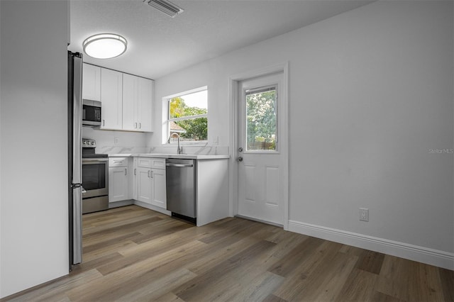 kitchen with light hardwood / wood-style flooring, white cabinets, a textured ceiling, and appliances with stainless steel finishes