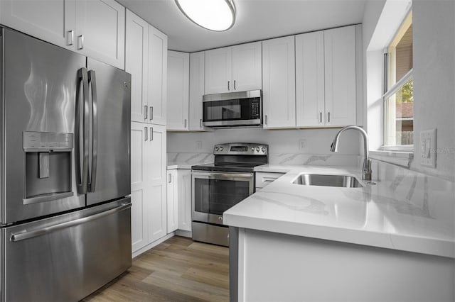 kitchen featuring sink, light wood-type flooring, appliances with stainless steel finishes, light stone counters, and white cabinetry