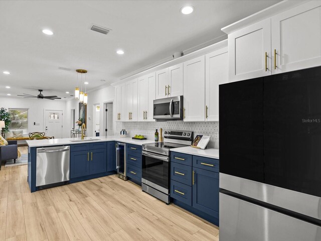 kitchen with pendant lighting, blue cabinets, ceiling fan, light hardwood / wood-style floors, and stainless steel appliances