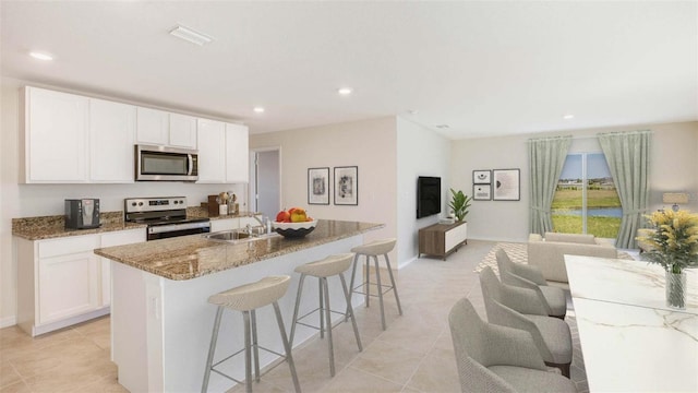 kitchen with light stone countertops, appliances with stainless steel finishes, a kitchen island with sink, sink, and white cabinetry