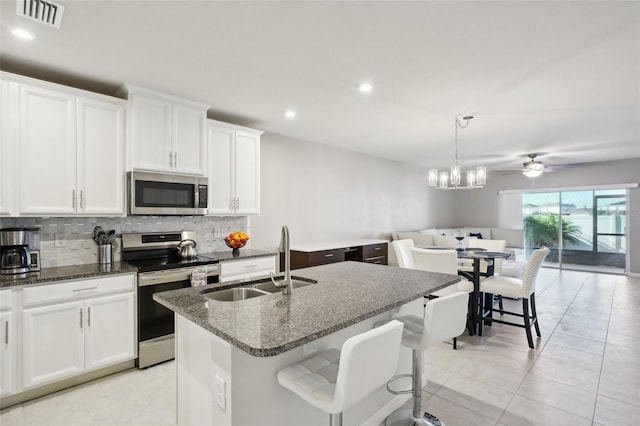 kitchen with appliances with stainless steel finishes, dark stone counters, sink, white cabinetry, and an island with sink