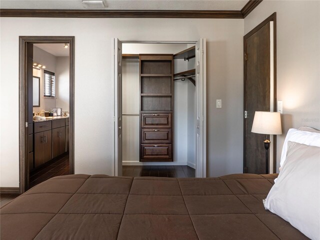 bedroom featuring baseboards, dark wood-style flooring, ornamental molding, a closet, and ensuite bathroom