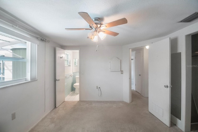 unfurnished bedroom with ensuite bath, ceiling fan, light carpet, and a textured ceiling