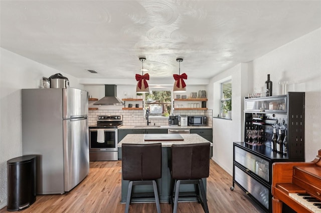 kitchen featuring a center island, wall chimney range hood, sink, decorative light fixtures, and stainless steel appliances