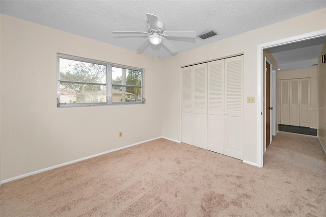 unfurnished bedroom with ceiling fan, a closet, light colored carpet, and a textured ceiling