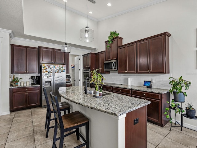 kitchen featuring light stone countertops, stainless steel appliances, a kitchen island with sink, sink, and hanging light fixtures