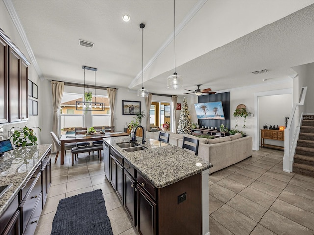 kitchen featuring a kitchen island with sink, dark brown cabinets, decorative light fixtures, and sink