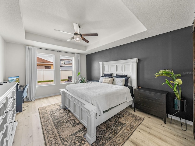 bedroom with light wood-type flooring, a tray ceiling, and ceiling fan