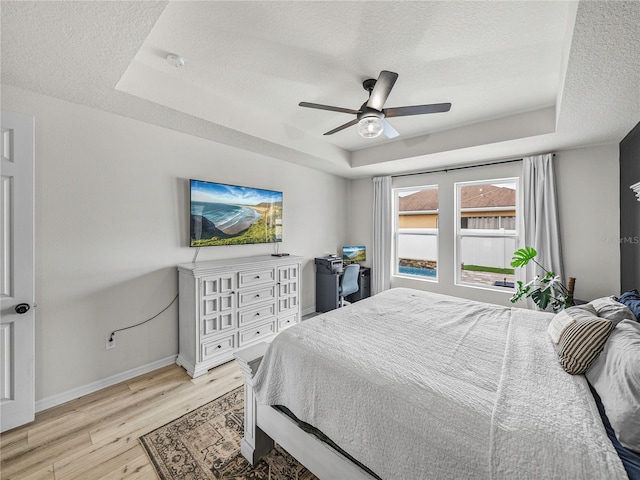 bedroom with ceiling fan, light hardwood / wood-style floors, a raised ceiling, and a textured ceiling