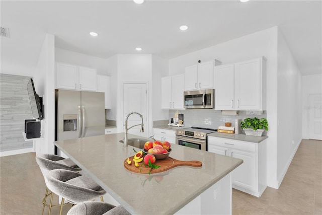 kitchen with sink, a breakfast bar, appliances with stainless steel finishes, an island with sink, and white cabinets