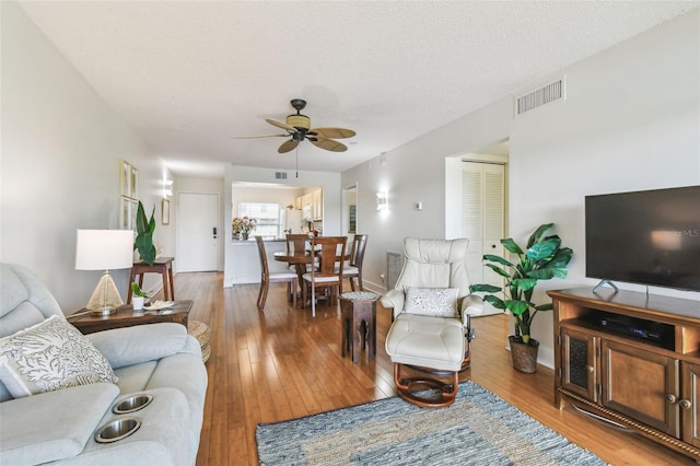 living room with ceiling fan, light wood-type flooring, and a textured ceiling