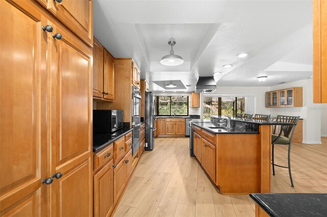 kitchen featuring light wood-type flooring, sink, decorative light fixtures, a center island with sink, and a breakfast bar area