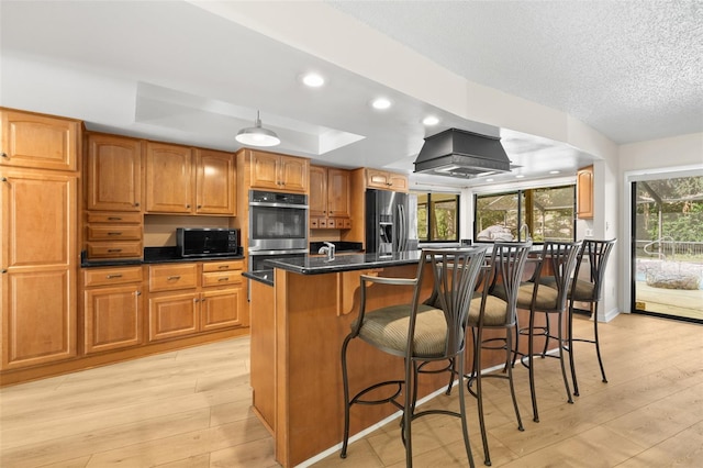 kitchen featuring light wood-type flooring, an island with sink, appliances with stainless steel finishes, and a tray ceiling