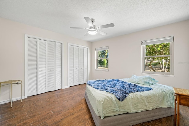 bedroom featuring ceiling fan, two closets, dark wood-type flooring, and multiple windows