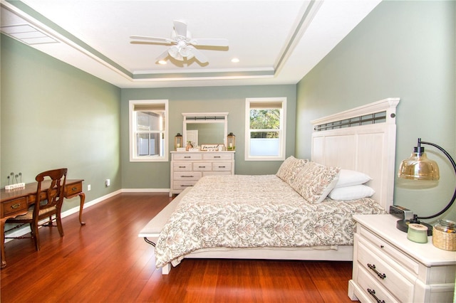 bedroom with a raised ceiling, ceiling fan, and dark wood-type flooring